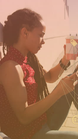 Globe-of-digital-icons-against-african-american-woman-using-smartphone-sitting-on-the-promenade