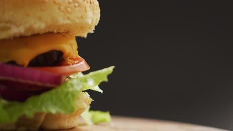 Vídeo-De-Primer-Plano-De-Una-Hamburguesa-Con-Queso-Y-Ensalada-En-Pan-De-Hamburguesa,-Sobre-Fondo-Gris-Con-Espacio-Para-Copiar