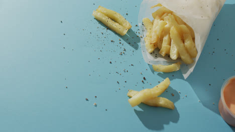 Video-of-chips-wrapped-in-paper,-salt-and-pepper-and-dip,-with-copy-space-on-blue-background