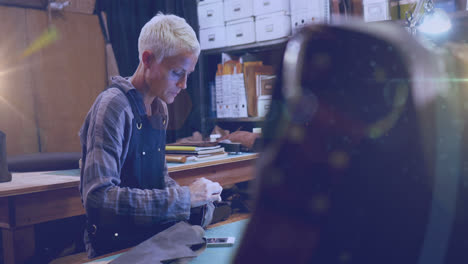 Animation-of-glowing-light-over-caucasian-woman-working-in-workshop