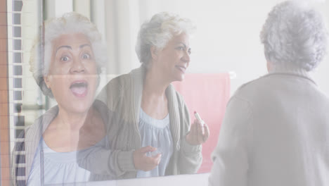 Composite-of-cheerful-senior-woman-in-mirror-putting-on-lipstick,-and-greeting-visitor-at-front-door