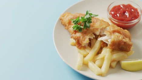 Vídeo-De-Primer-Plano-De-Pescado-Y-Patatas-Fritas,-Perejil-Y-Plato-De-Salsa-De-Tomate-En-Un-Plato,-Con-Espacio-Para-Copiar-En-Azul