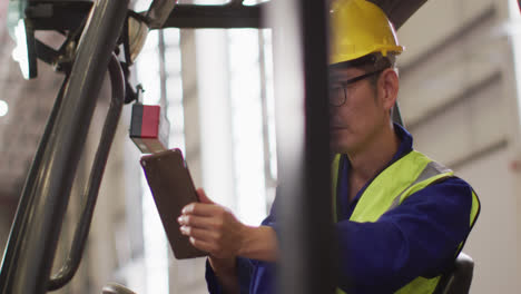 Asiatischer-Männlicher-Arbeiter-Trägt-Sicherheitsanzug-Mit-Helm-Und-Benutzt-Tablet-Im-Lager