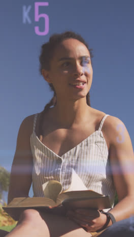 Animation-of-letters-and-numbers-over-smiling-biracial-woman-reading-in-park