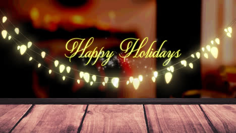 Animation-of-fairy-lights-and-happy-holidays-text-over-wooden-boards