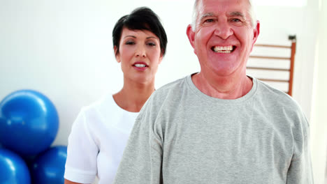 Smiling-physiotherapist-helping-elderly-patient-lift-hand-weights