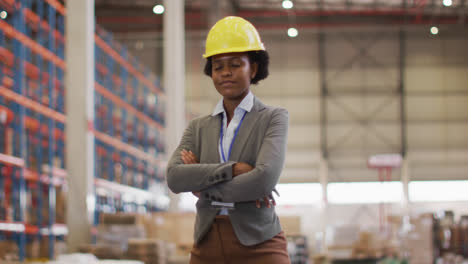 Portrait-of-african-american-female-worker-wearing-helmet-and-smiling-in-warehouse