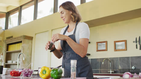 Happy-caucasian-pregnant-woman-cooking,-using-seasons-in-kitchen