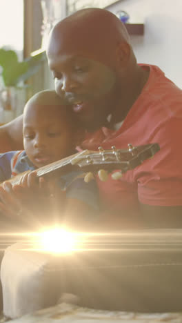 Animación-De-Puntos-De-Luz-Sobre-Un-Feliz-Padre-Afroamericano-Tocando-La-Guitarra-Con-Su-Hijo