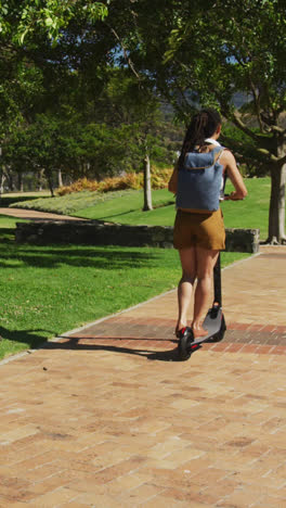 Multiple-green-leaves-icons-against-african-american-woman-riding-electric-scooter-in-the-park