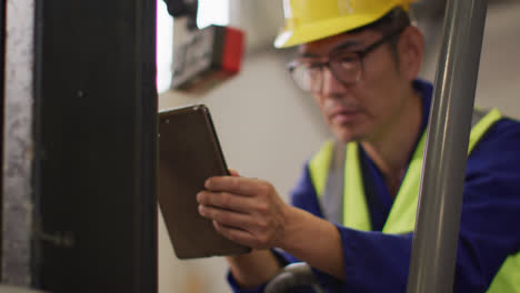 Asiatischer-Männlicher-Arbeiter-Trägt-Sicherheitsanzug-Mit-Helm-Und-Benutzt-Tablet-Im-Lager