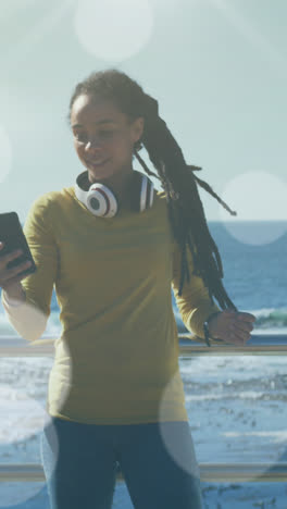 Animation-Von-Lichtpunkten-über-Einer-Frau-Mit-Gemischter-Abstammung,-Die-Auf-Der-Promenade-Ein-Smartphone-Benutzt