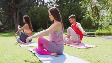 Grupo-Diverso-De-Hombres-Y-Mujeres-Practicando-Yoga-Sentados-En-Esteras-En-El-Parque-Soleado