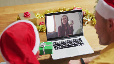 Kaukasischer-Vater-Und-Sohn-Mit-Weihnachtsmützen-Mit-Laptop-Für-Weihnachtsvideoanruf-Mit-Frau-Auf-Dem-Bildschirm