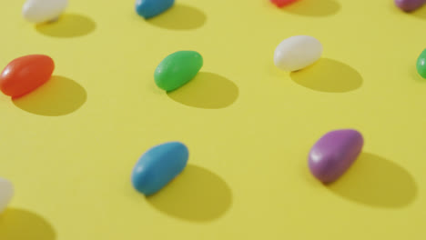 Video-of-close-up-of-rows-of-multi-coloured-sweets-over-yellow-background