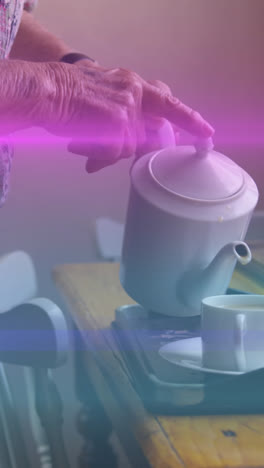 Animation-of-coloured-lights-moving-over-senior-woman-pouring-tea-at-home
