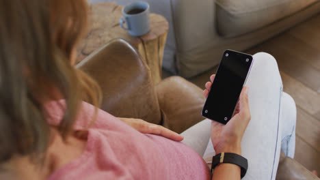 Happy-caucasian-pregnant-woman-sitting-in-armchair-and-using-smartphone-with-copy-space