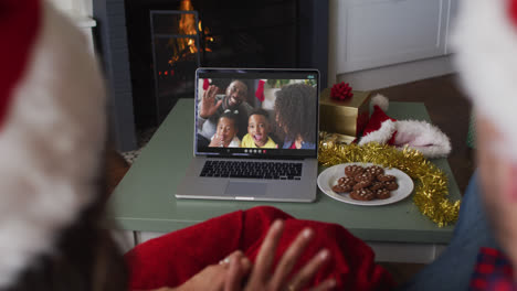 Rückansicht-Eines-Kaukasischen-Paares-Mit-Weihnachtsmützen,-Das-Während-Der-Weihnachtszeit-Einen-Videoanruf-Auf-Dem-Laptop-Führt