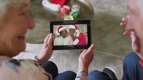 Pareja-Caucásica-Mayor-Usando-Tableta-Para-Videollamada-Navideña-Con-Pareja-Feliz-En-Pantalla