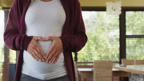 Midsection-of-caucasian-pregnant-woman-gesturing-heart-over-belly