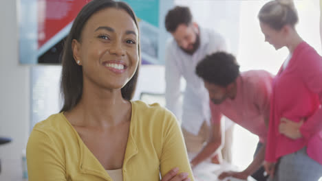 Portrait-of-happy-biracial-businesswoman-over-diverse-colleagues-in-office