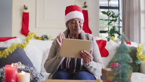 Feliz-Mujer-Mayor-Afroamericana-Con-Sombrero-Navideño-De-Papá-Noel-Haciendo-Videollamadas-Con-Tabletas,-Cámara-Lenta