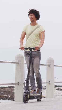 Young-biracial-man-rides-an-electric-scooter-on-a-pier,-with-copy-space