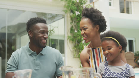 Happy-african-american-family-talking-and-having-breakfast-in-garden