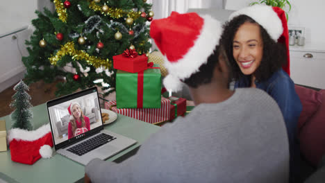 African-american-couple-wearing-santa-hats-having-a-videocall-on-laptop-at-home-during-christmas