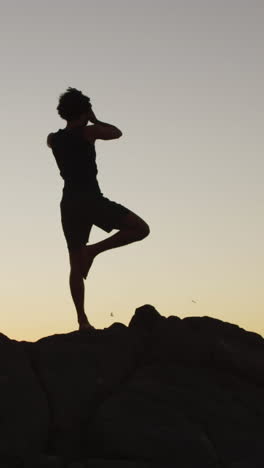 Un-Joven-Birracial-Silueteado-Practica-Yoga-Al-Aire-Libre-Al-Atardecer