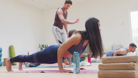 Diverse-group-practicing-yoga-pose-in-class-with-male-instructor-helping