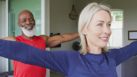 Mixed-race-senior-couple-performing-stretching-exercise-together-at-home