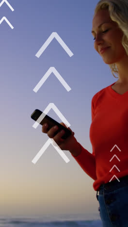 Animation-of-arrows-over-happy-caucasian-woman-using-smartphone-at-sunset