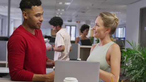 Happy-diverse-male-and-female-business-colleagues-talking-and-using-laptop