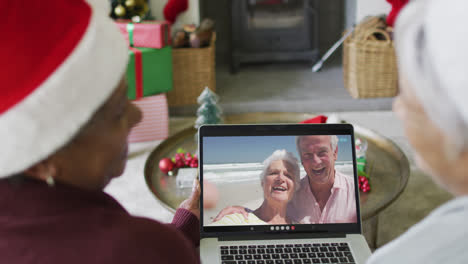 Diverse-senior-female-friends-using-laptop-for-christmas-video-call-with-happy-couple-on-screen