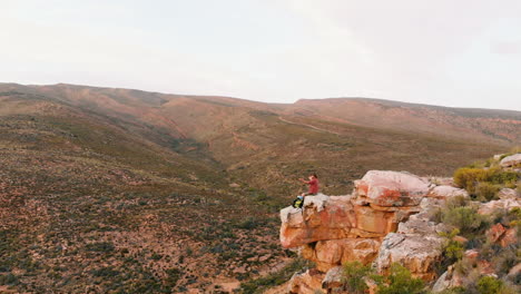 Young-Caucasian-man-sits-on-a-cliff-edge,-outdoor-with-copy-space