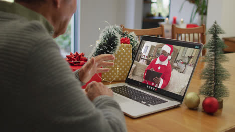 Hombre-Mayor-Caucásico-Que-Tiene-Videollamada-Navideña-En-Una-Computadora-Portátil-Con-Santa-Afroamericano-Con-Máscara-Facial