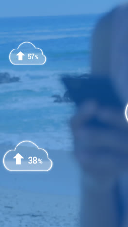 Animation-of-clouds-with-arrows-and-percent-going-up-over-caucasian-woman-using-smartphone