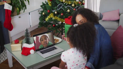 African-american-mother-and-daughter-having-a-videocall-on-laptop-at-home-during-christmas