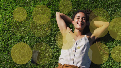 Animación-De-Manchas-Amarillas-Sobre-Una-Mujer-Birracial-Sonriente-Tumbada-En-El-Parque