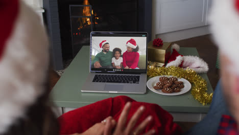 Rückansicht-Eines-Kaukasischen-Paares-Mit-Weihnachtsmützen,-Das-Während-Der-Weihnachtszeit-Einen-Videoanruf-Auf-Dem-Laptop-Führt