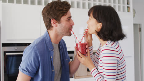 Video-De-Una-Feliz-Pareja-Diversa-Bebiendo-Jugo-Con-Pajitas-En-La-Cocina