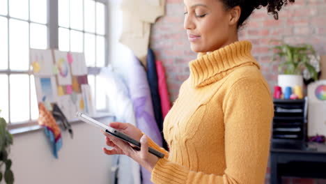 Happy-biracial-female-fashion-designer-using-tablet-at-studio-and-smiling,-slow-motion