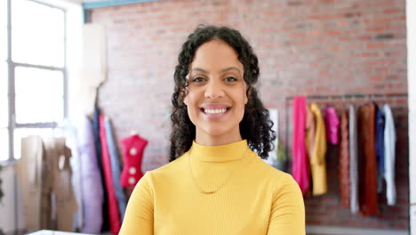 Retrato-De-Una-Diseñadora-De-Moda-Birracial-Con-Pelo-Rizado-Oscuro-Sonriendo-En-El-Estudio,-Cámara-Lenta