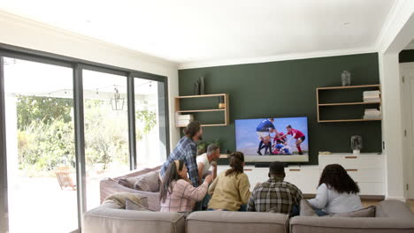 Happy-diverse-male-and-female-friends-watching-sport-on-tv-and-celebrating-victory