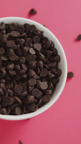 Video-of-overhead-view-of-bowl-of-chocolate-chip-over-pink-background