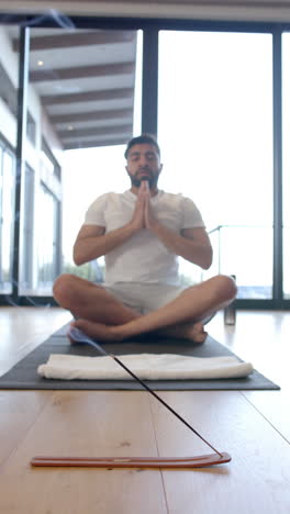 Vertical-video-of-biracial-man-doing-yoga-and-meditating-at-home,-slow-motion
