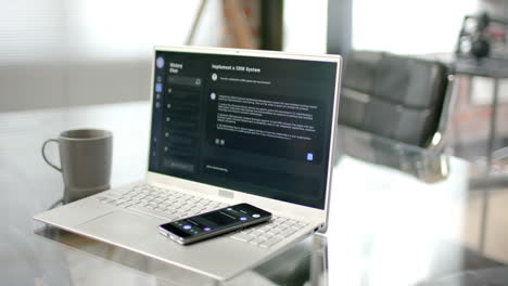 Close-up-of-desk-with-smartphone,-laptop-with-ai-chatbot-and-mug-of-coffee-at-home,-slow-motion