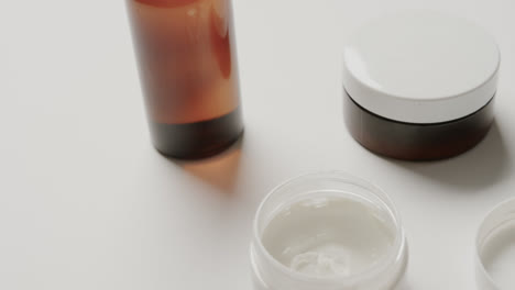 Close-up-of-cream-tubs-and-glass-bottle-with-copy-space-on-white-background