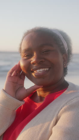 Vídeo-Vertical-De-Retrato-De-Una-Feliz-Mujer-Afroamericana-Sonriendo-En-La-Playa,-En-Cámara-Lenta